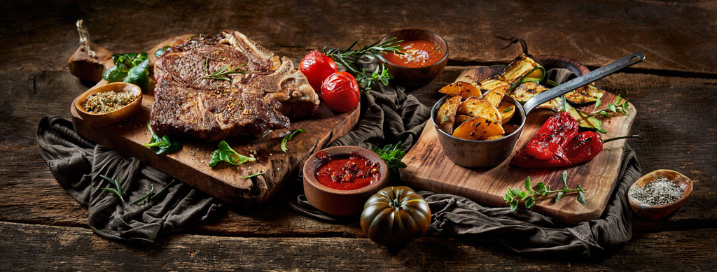 Barbecue recipes: beef steak with grilled potato wedges, grilled vegetables, dips and spices presented on a wooden board