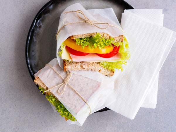Sandwiches with ham, cheese, peppers and lettuce in wrapping paper and natural cord