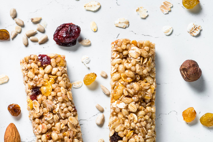 Two muesli bars on a white background with nuts and berries around them